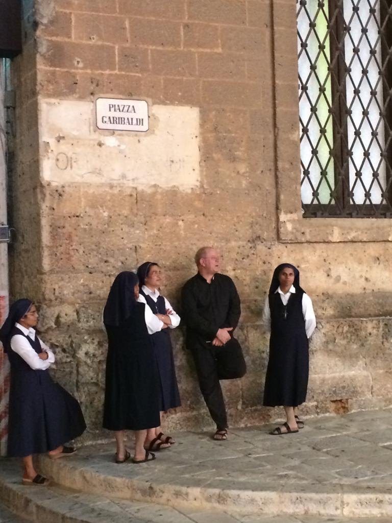 A priest and nuns waiting in the shade in Piazza Garibaldi, Manduria, Salento, Puglia